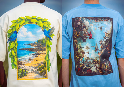 Two models shown from the back wearing graphic t-shirts. The left model wears a cream-colored t-shirt with a large back graphic depicting a tropical beach scene framed by a green laurel wreath and blue birds.